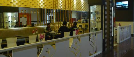 Un restaurant moderne doté d’un plafond aux motifs géométriques, d’un comptoir avec un miroir et d’un espace salon agrémenté d’une cloison décorative.