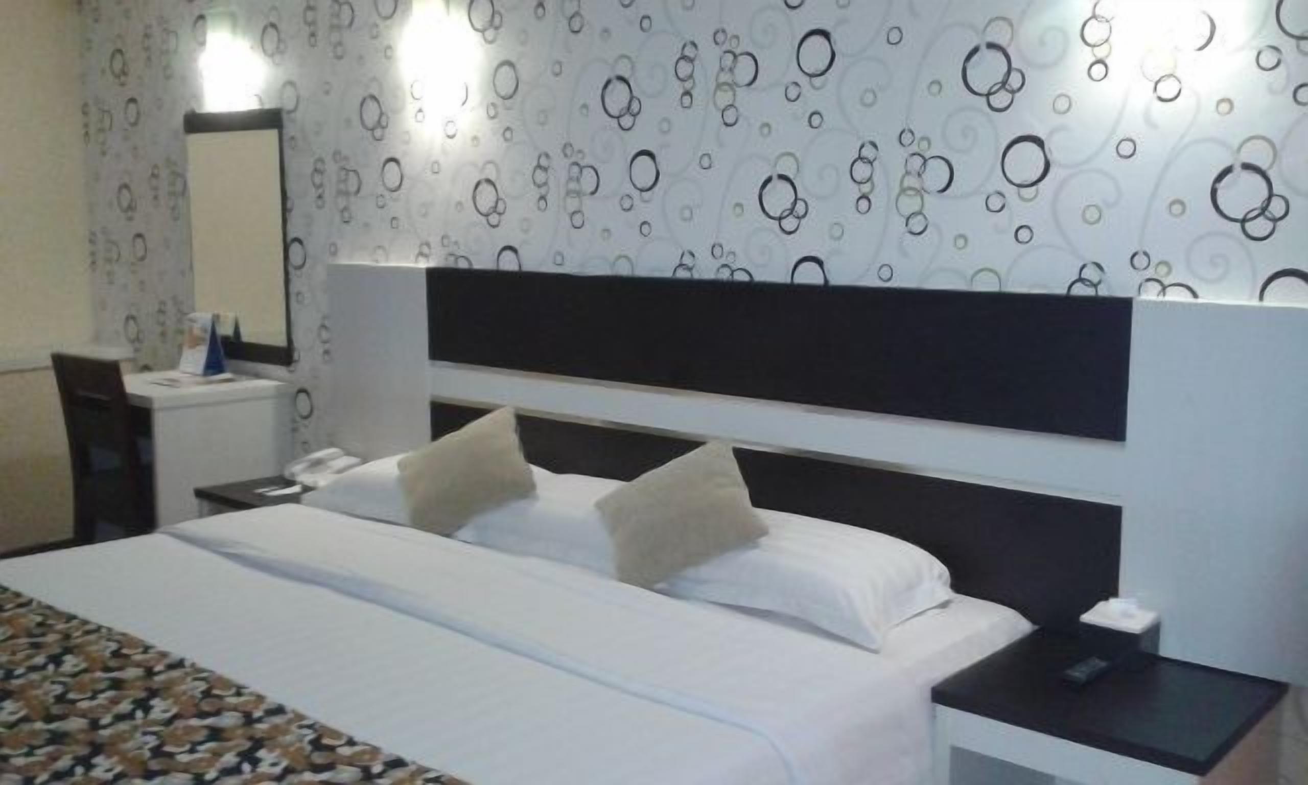 Une chambre d’hôtel avec un lit, une table de chevet, un miroir et un mur décoré d’un motif.