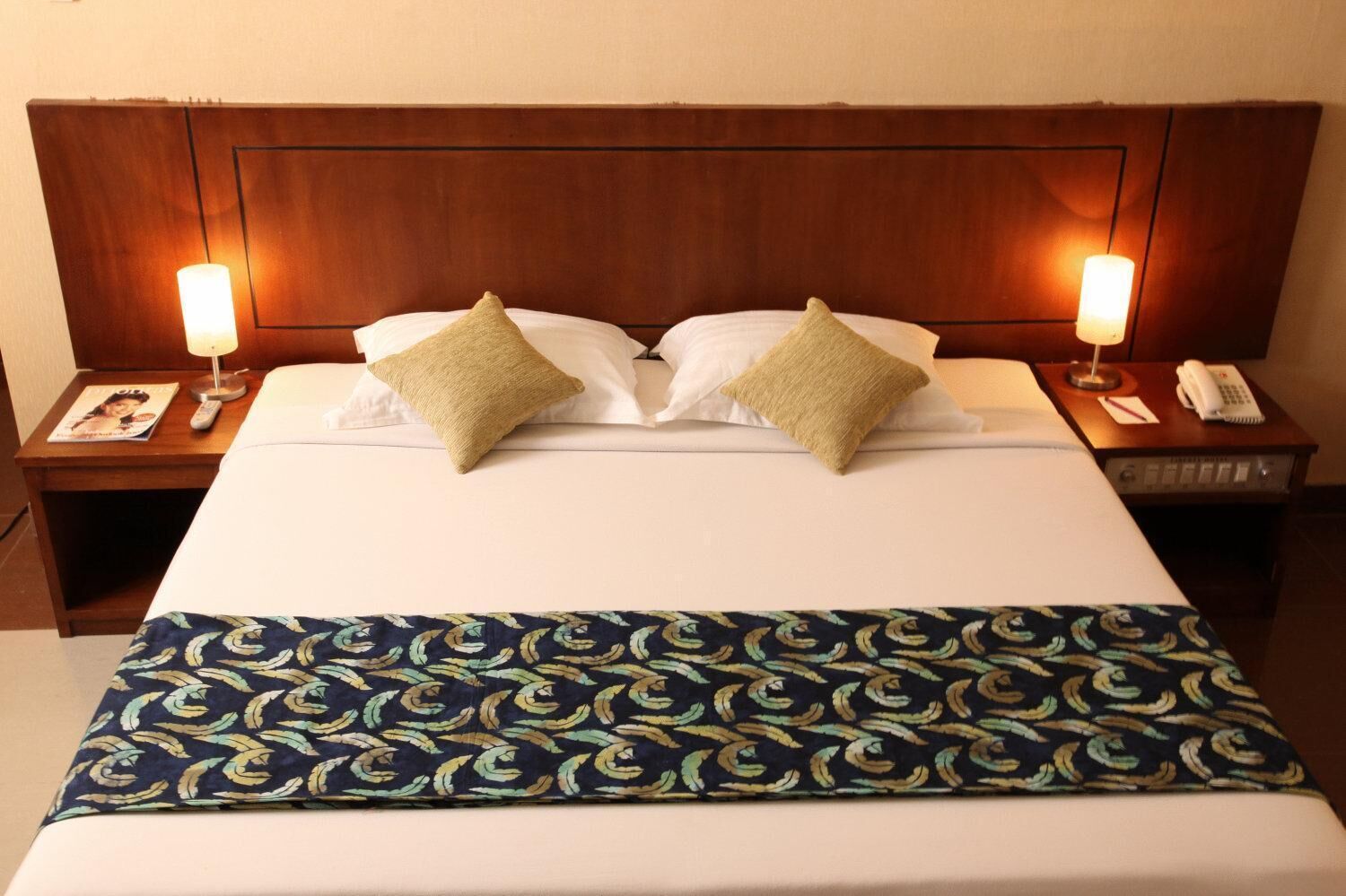 A hotel room with a large bed, two bedside lamps, a telephone, and a magazine on the nightstand.