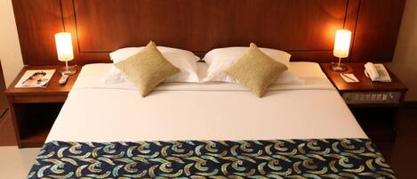 A hotel room with a large bed, two bedside lamps, a telephone, and a magazine on the nightstand.