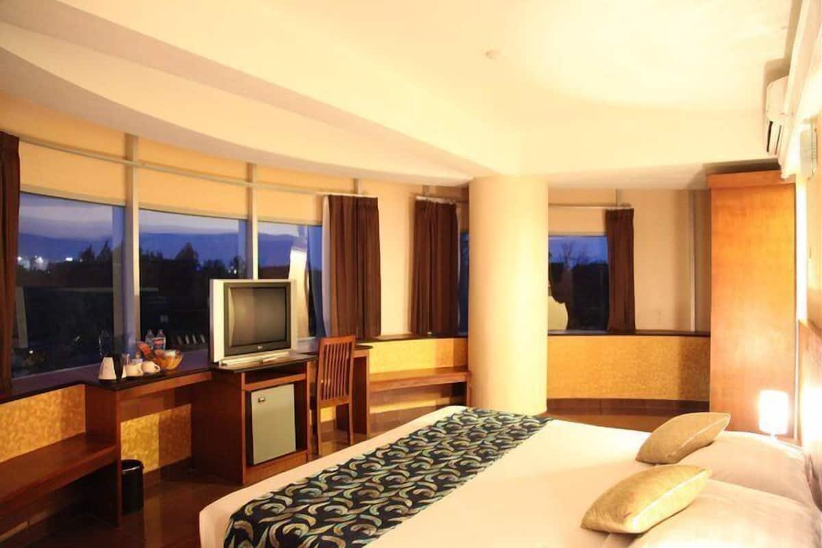 Ein Hotelzimmer mit einem Bett, einem Schreibtisch mit Fernseher und großen Fenstern.