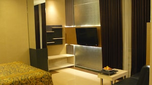 A hotel room with a bed, a small table with fruit, a sofa, and a TV on the wall.