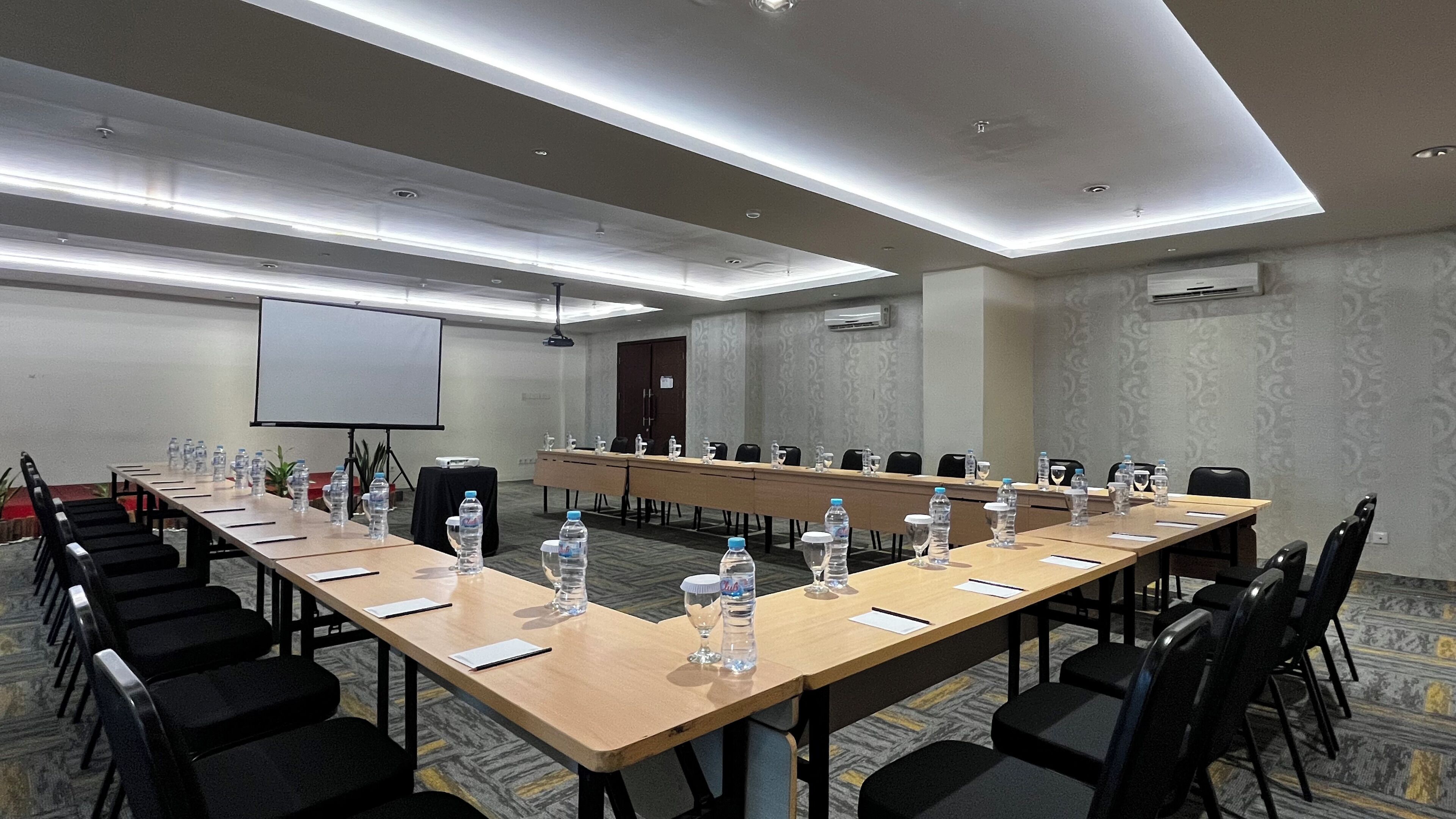 A conference room with a long table, chairs, water bottles, and a projector screen.