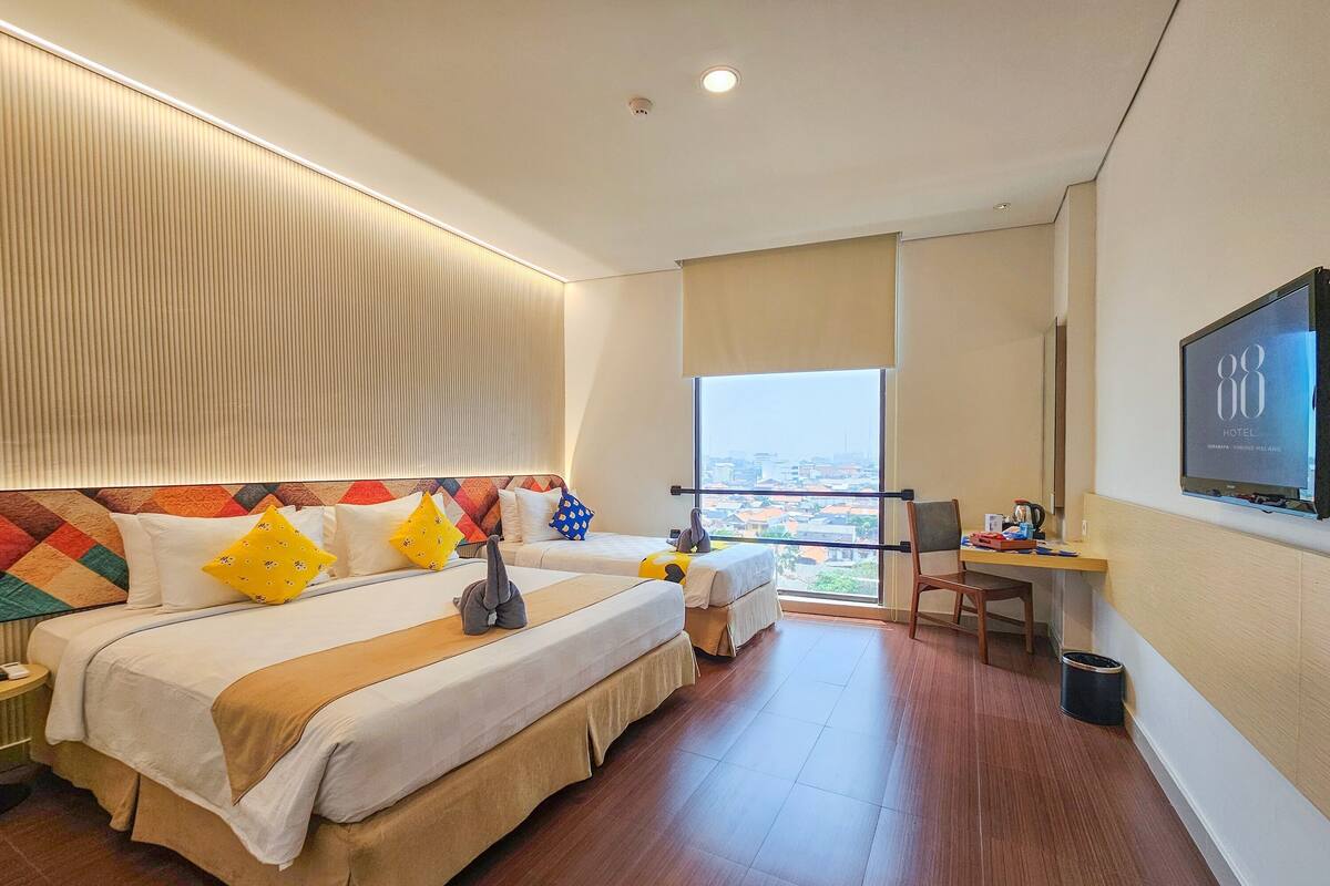 A hotel room with a large bed, a desk, a TV, and a view of the city.