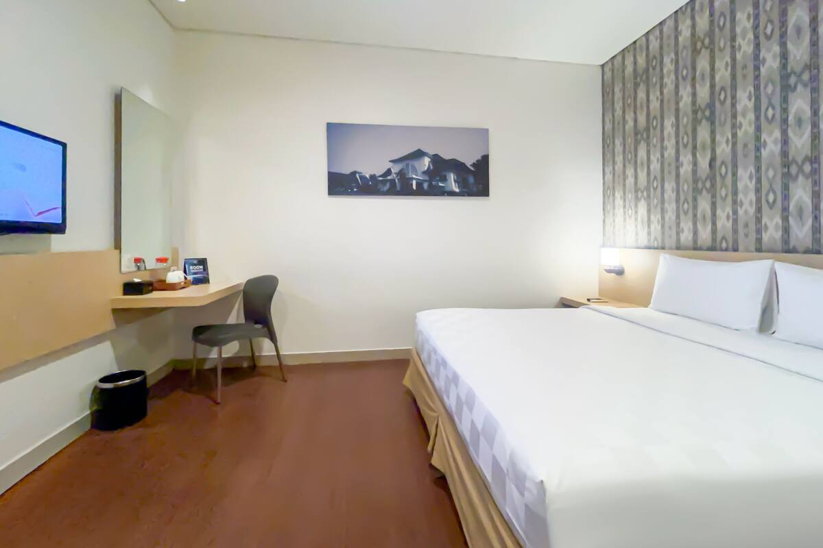 A hotel room with a bed, a desk with a chair, a television, and a picture on the wall.