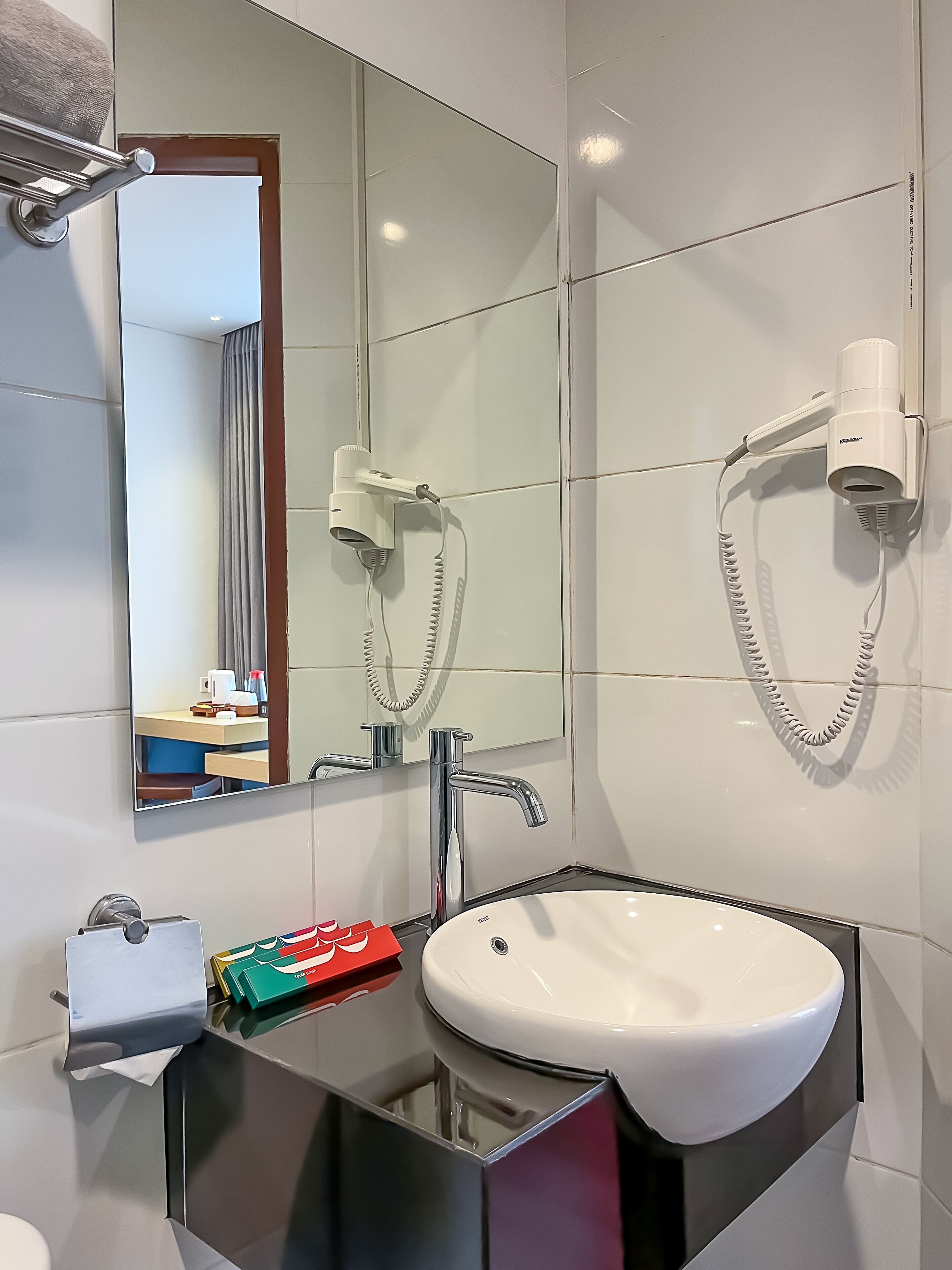Un baño moderno con un espejo grande, un lavamanos blanco y dos secadores de pelo montados en la pared.