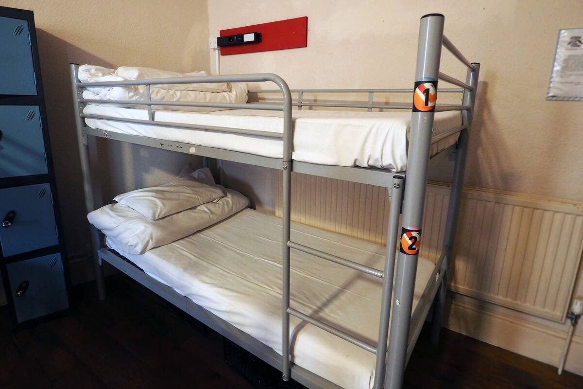 Uma cama beliche com dois níveis, uma placa de saída de emergência vermelha e um radiador branco na parede.