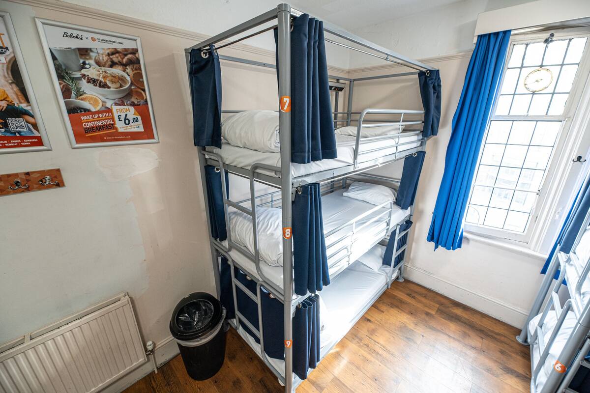 Quarto com beliche, um quadro na parede, janela com cortinas e radiador.