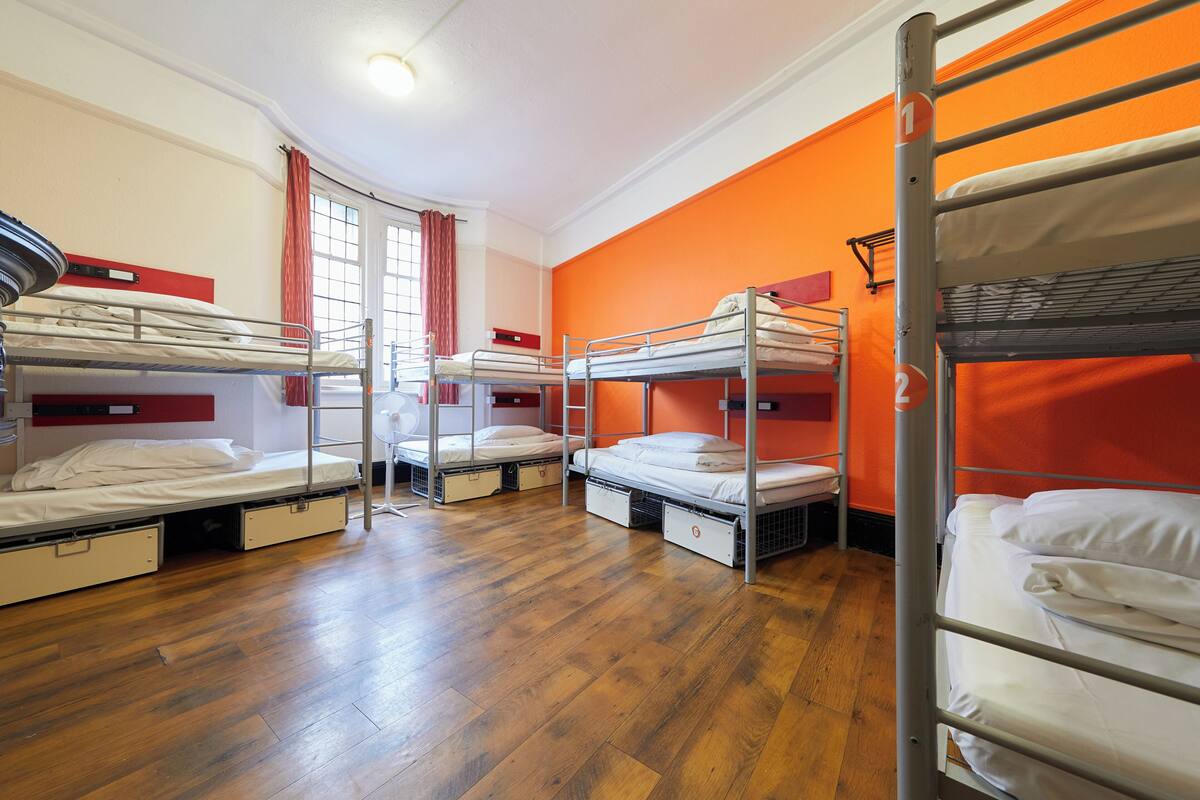 Quarto de dormitório com beliches, piso de madeira e paredes laranja.