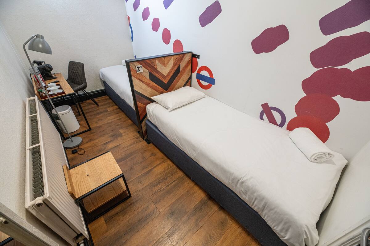 Quarto pequeno e bem arrumado, com cama, escrivaninha, cadeira e radiador.