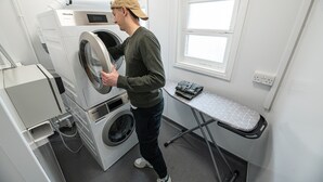 A compact laundry room with a front-loading washing machine, a drying machine, and a small ironing station with an ironing board and iron. - St Christopher's Inn Hammersmith (London)