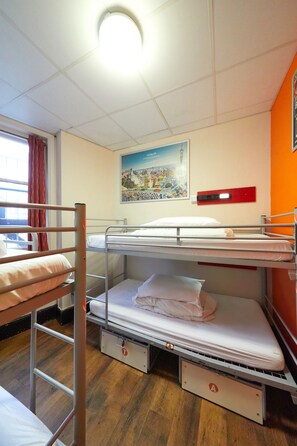 A dormitory room with bunk beds, a poster on the wall, and a window with curtains.