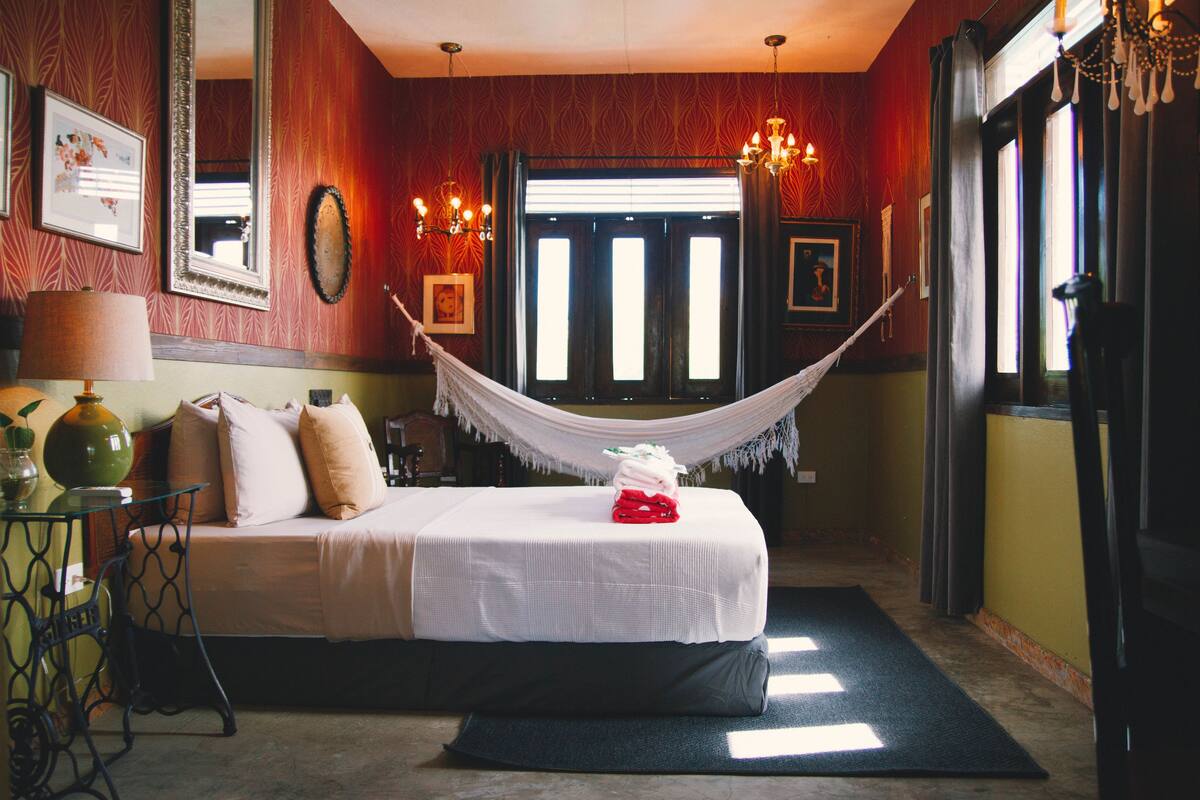 Ein Hotelzimmer mit Bett, Hängematte, Schreibtisch und einem Fenster mit Vorhängen.