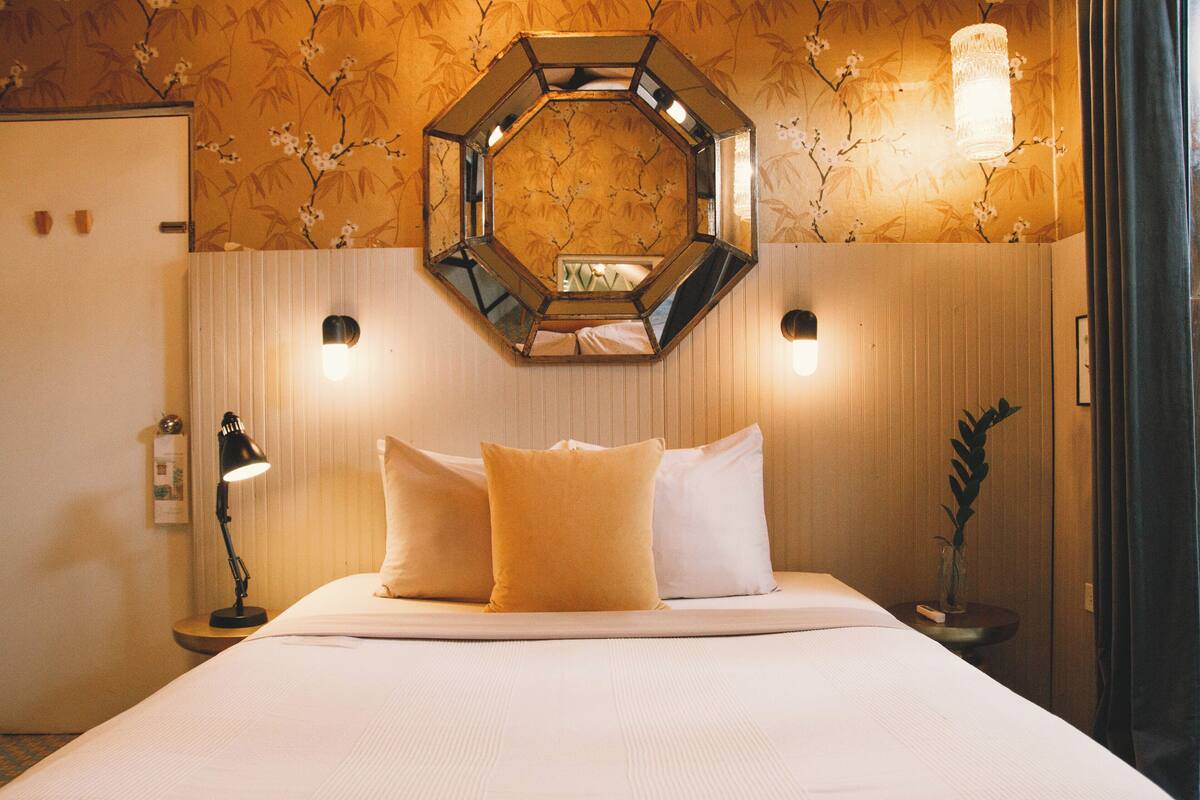 Ein Hotelzimmer mit einem großen Bett, zwei Nachttischlampen, einem dekorativen Spiegel über dem Bett und einer Wand mit floralem Wandpapier.