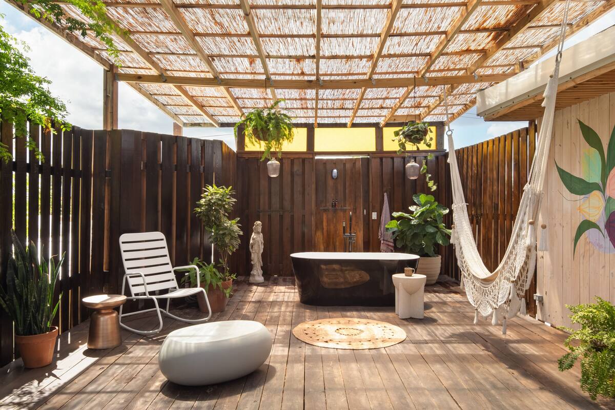Eine Holzterrasse mit einer Pergola, einem Whirlpool, einer Statue und verschiedenen Blumentöpfen.