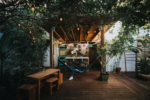 Eine Hängematte unter einer Holz-Pergola mit hängenden Lichtern, umgeben von Topfpflanzen und Holzmöbeln.