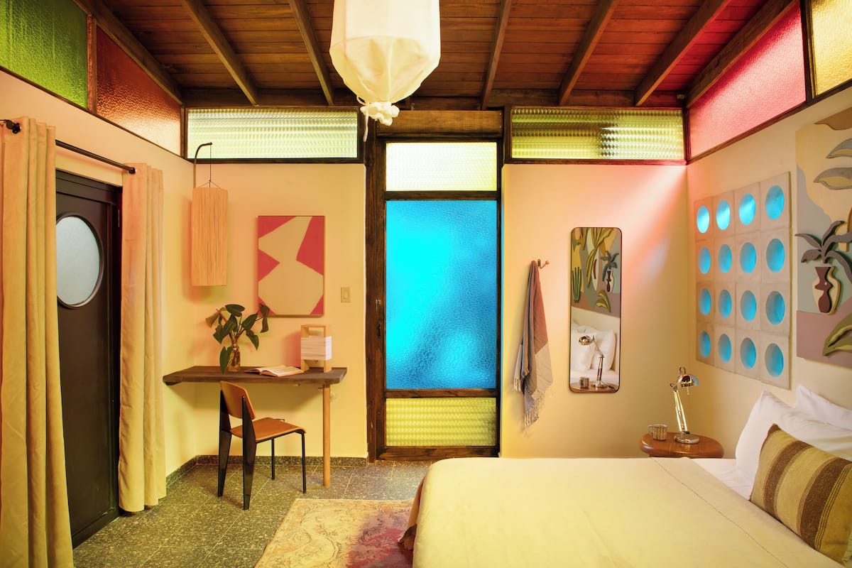Ein Hotelzimmer mit Bett, Schreibtisch mit Stuhl, kleinem Tisch mit Lampe und Fenster mit Aussicht.