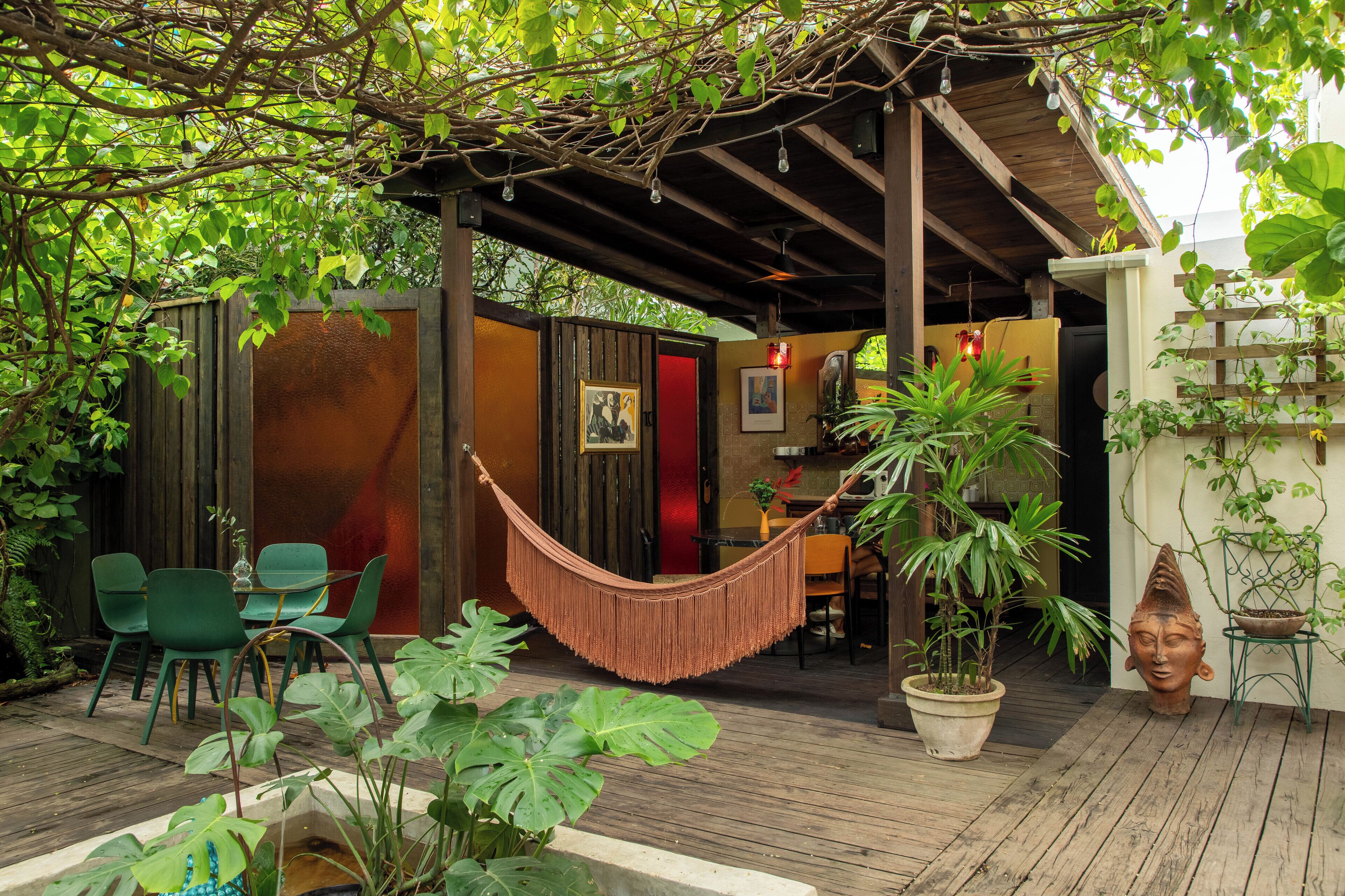 A wooden deck with a hammock, green chairs, and potted plants.