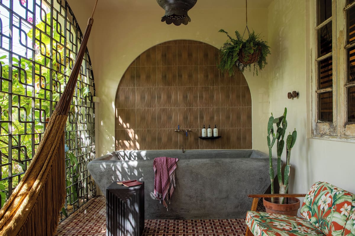Ein Zimmer mit einer Hängematte, einer Badewanne, einem Sofa und einem Blumentopf.