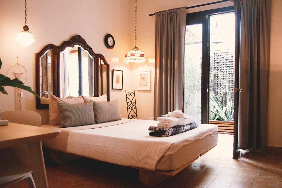 Ein Hotelzimmer mit Bett, Schreibtisch, Stuhl, Spiegel, einer Uhr und einem Fenster mit Vorhängen.