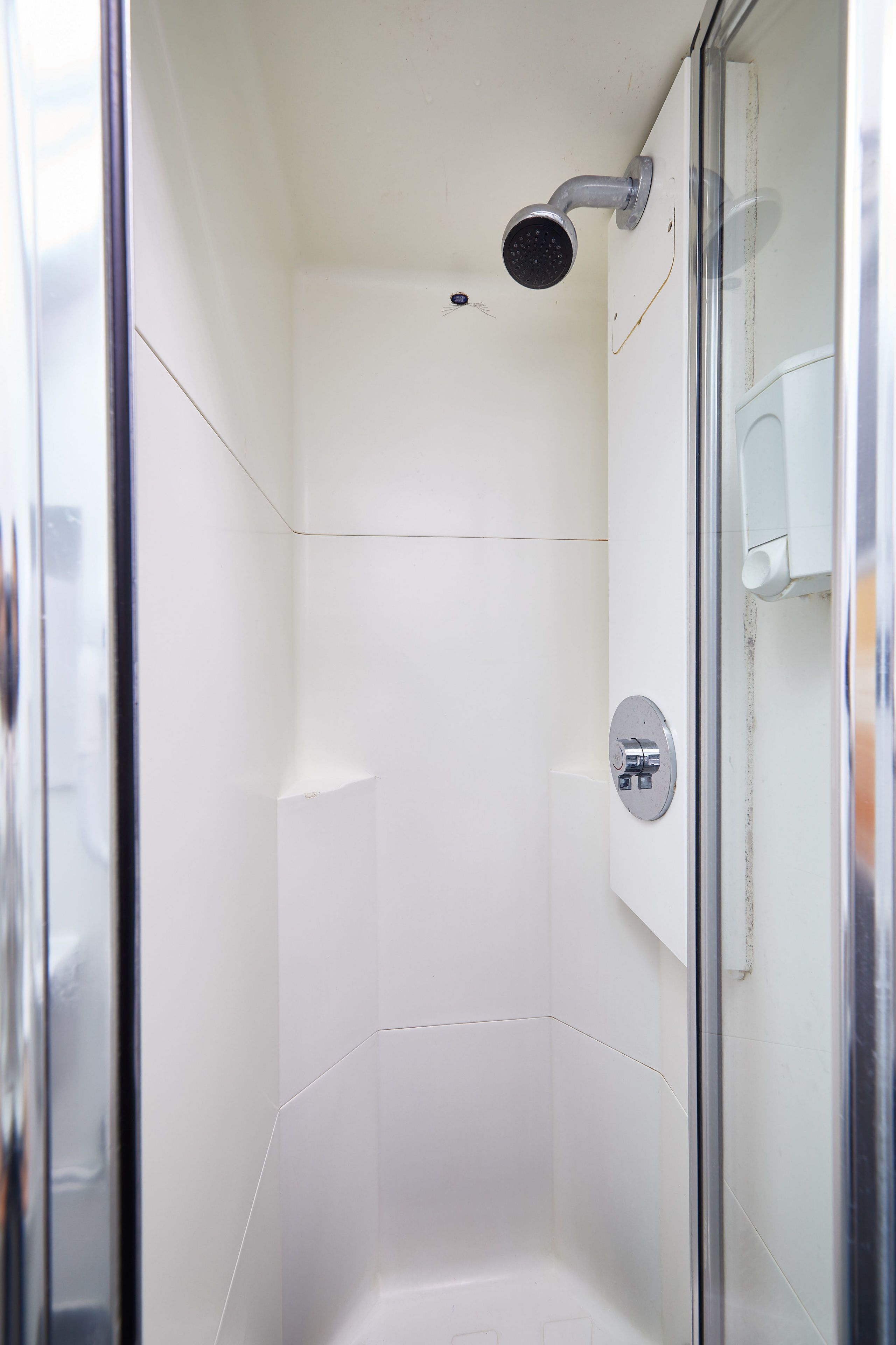 Una ducha moderna con puerta de vidrio, cabezal de ducha de mano y una perilla de control visible.