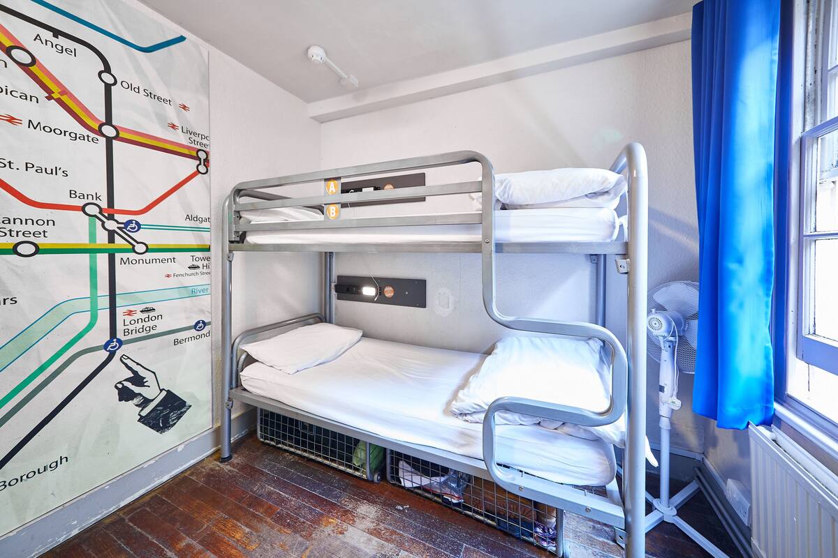 A bunk bed room with a map on the wall, a window with blue curtains, and a radiator.
