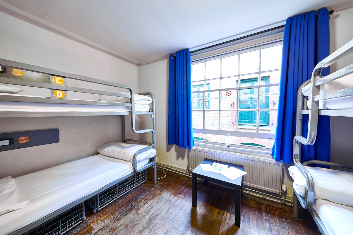 A room with bunk beds, a small table, and a window with blue curtains.