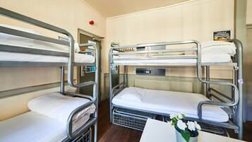 A bunk bed room with three levels, a sign for unlimited continental breakfast, and a flower vase on the table.