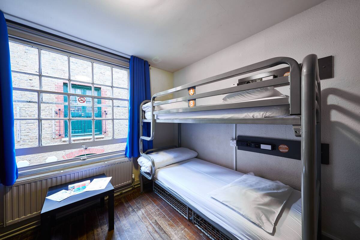 A bunk bed room with a window, a radiator, and a table with papers.
