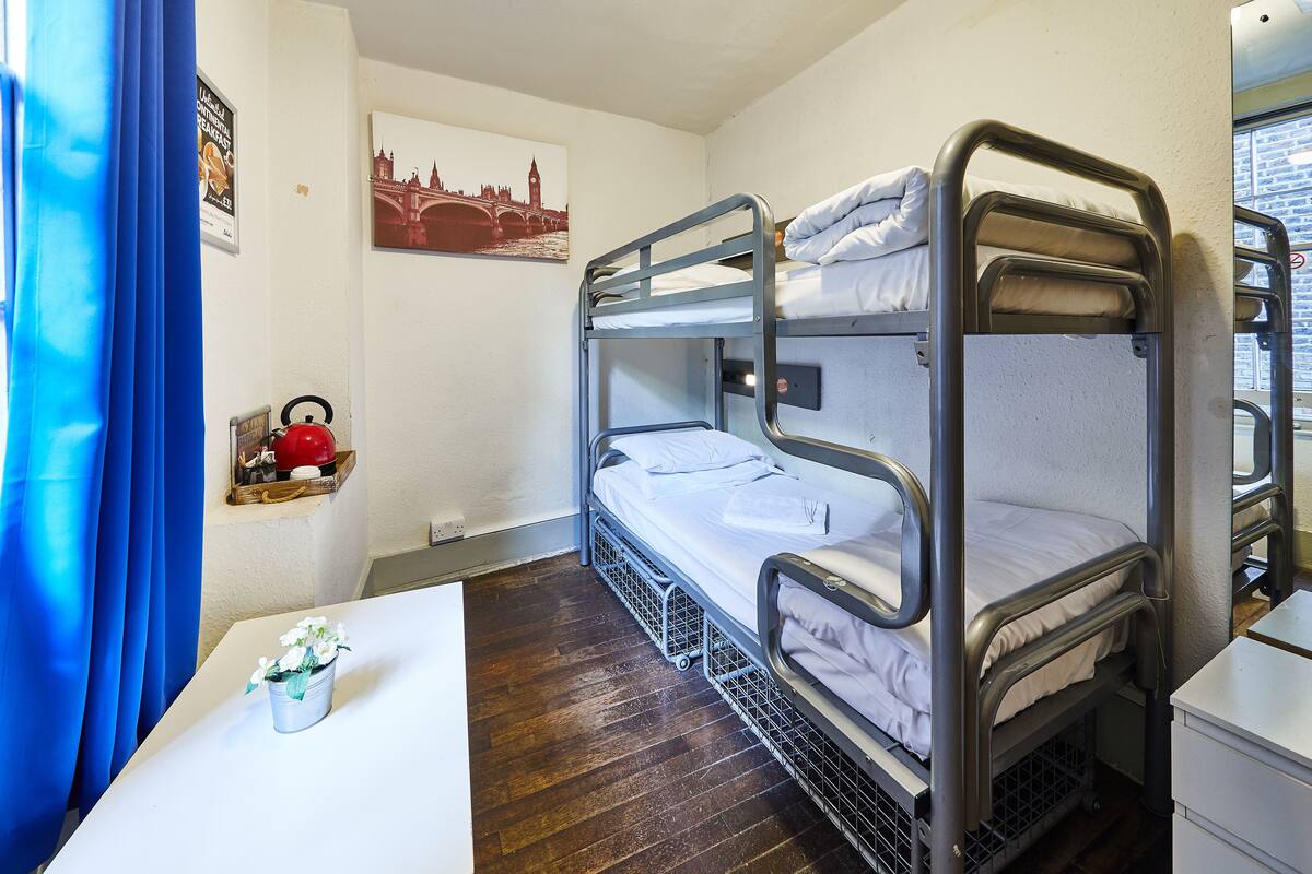 A bunk bed room with a small table, a kettle, and a picture of a bridge.
