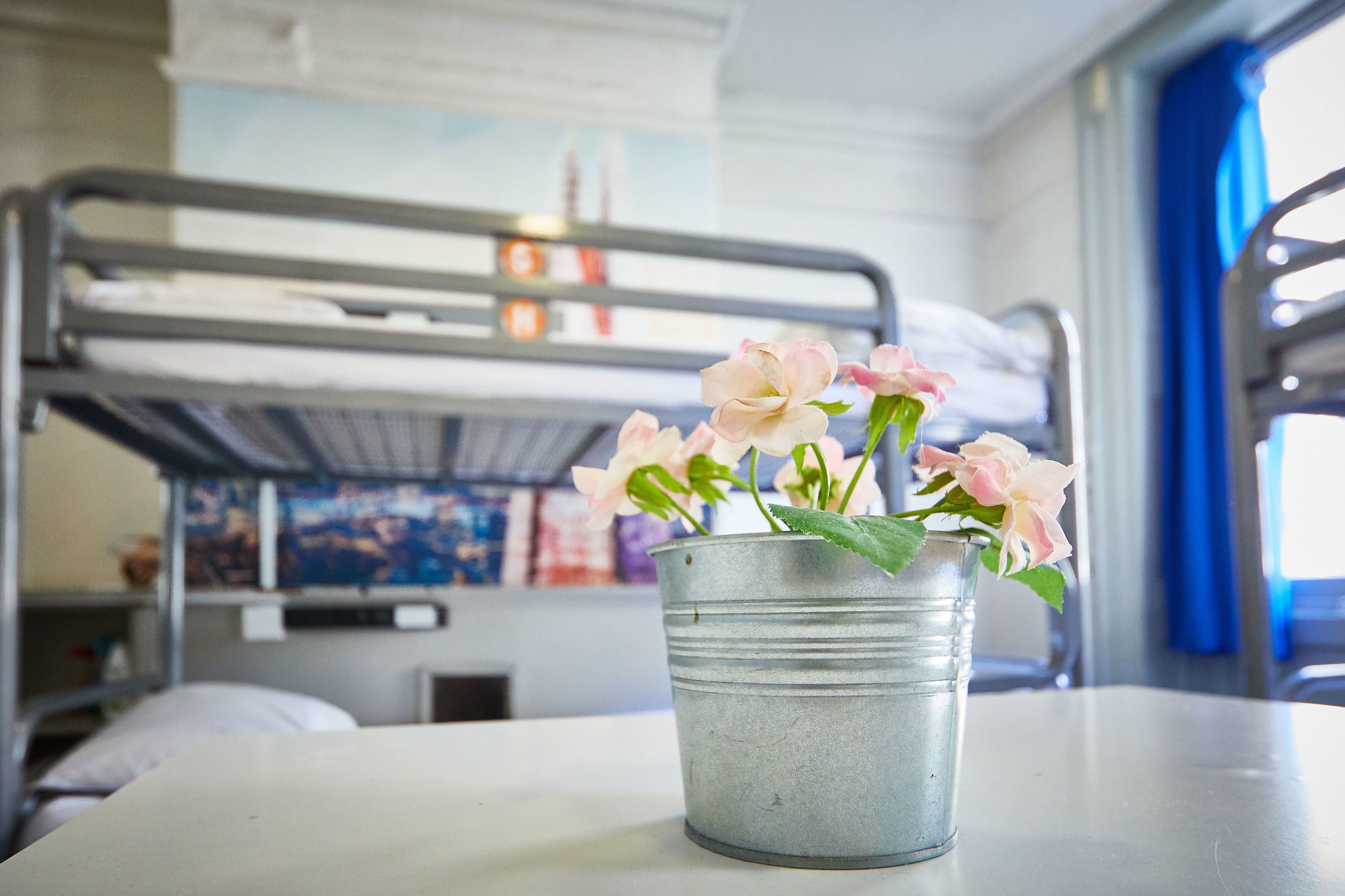 En køjeseng med en metalspand, der indeholder lyserøde blomster, på et bord.