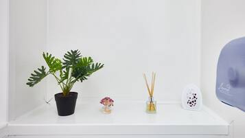 A white shelf with a potted plant, a small flower vase, and two reed diffuser containers.
