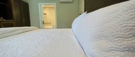 Een slaapkamer met een groot bed, een houten kledingkast en een badkamer die door een open deur zichtbaar is.