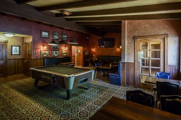 A billiards room with a pool table, seating, and framed pictures on the walls.