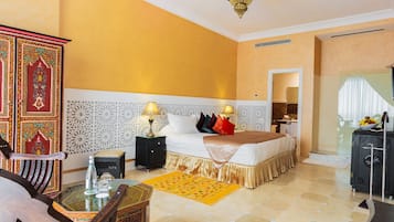 A hotel room with a bed, bedside tables, a nightstand, a decorative cabinet, a glass table with a bottle and glasses, and a yellow rug.
