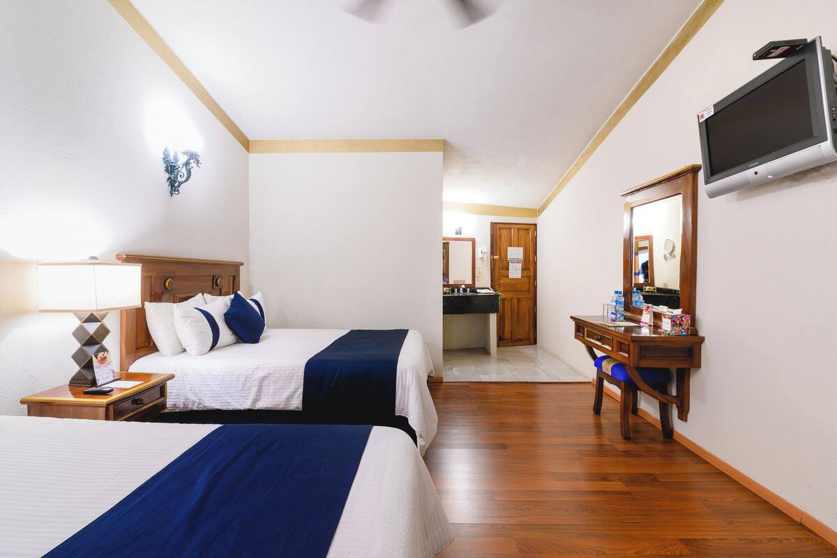 A hotel room with two beds, a desk, a TV, and a bathroom visible through an open door.