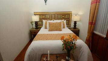 Habitación de hotel con una cama grande, dos mesitas de noche, una lámpara de pared, suelo de madera y una ventana con cortinas.