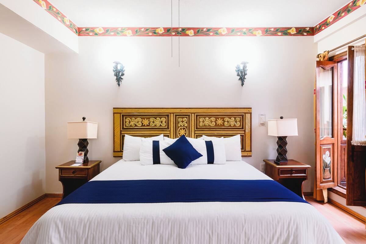 A hotel room with a large bed, two bedside tables, and a decorative headboard.