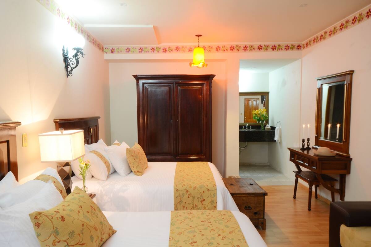 A hotel room with a large bed, a desk, a wardrobe, and a mirror.