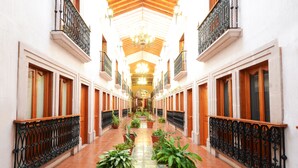 A corridor with tiled floors, potted plants, wooden doors, and black wrought iron railings. - Mision Patzcuaro Centro Historico (Patzcuaro)