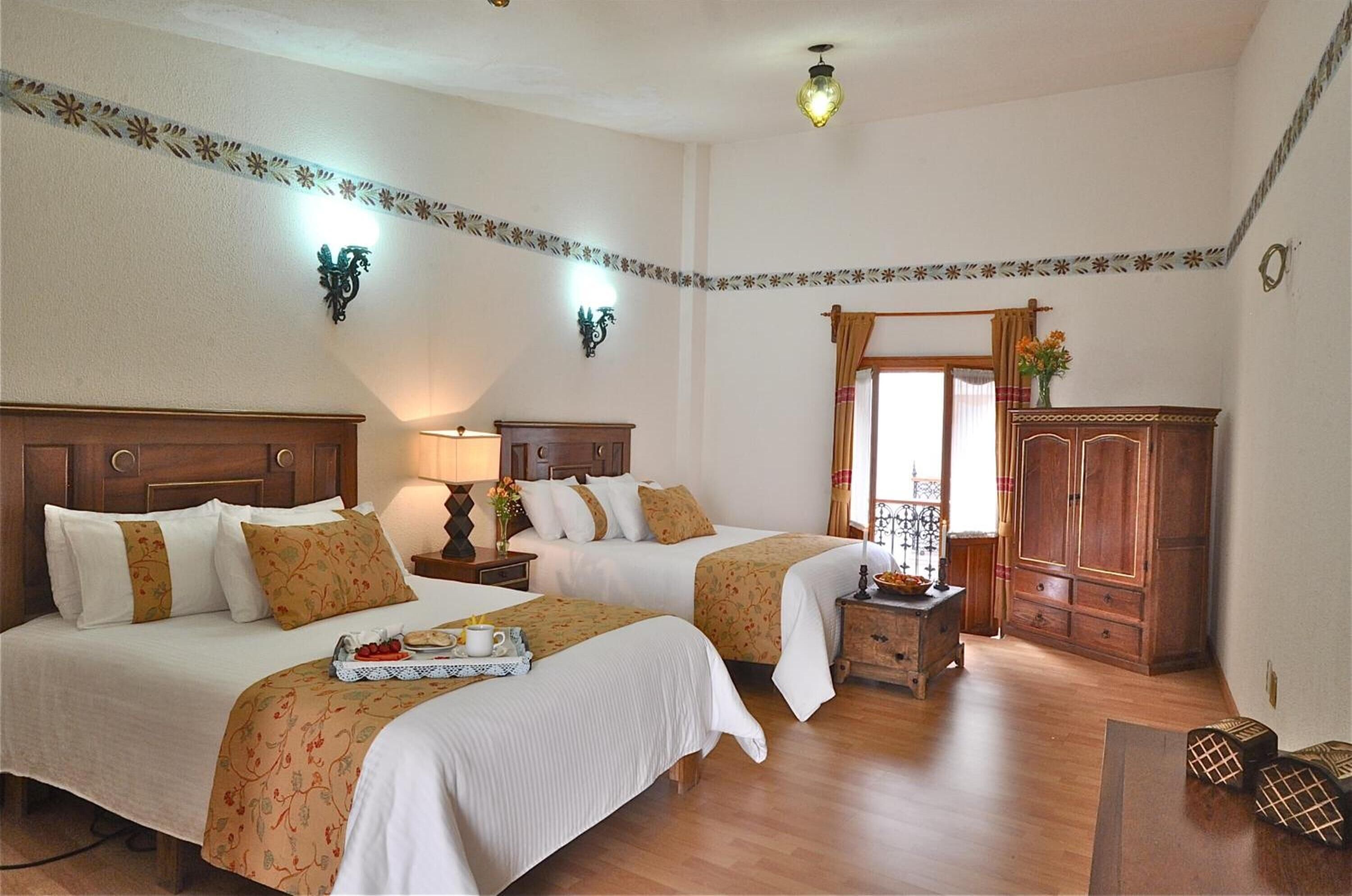 Habitación de hotel con dos camas, muebles de madera, un armario y un detalle decorativo en las paredes.