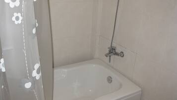 A bathroom with a bathtub, a showerhead, and a curtain with a floral pattern.