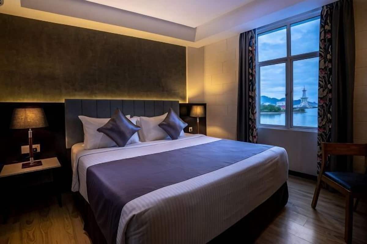 Une chambre dâhĂŽtel avec un grand lit, des tables de chevet avec des lampes, une vue sur un plan dâeau et un fauteuil.