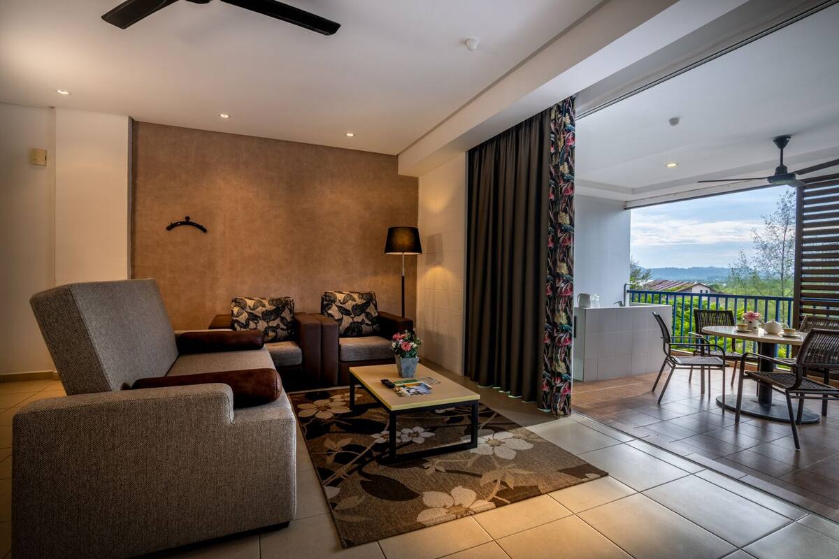 Un salon moderne avec un canapé, un fauteuil et une table basse, un balcon avec un coin salon extérieur et une vue sur la campagne.