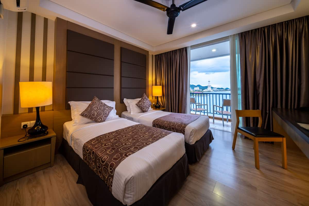 Une chambre d’hôtel avec deux lits, un ventilateur de plafond, un balcon avec vue et un bureau avec une chaise.