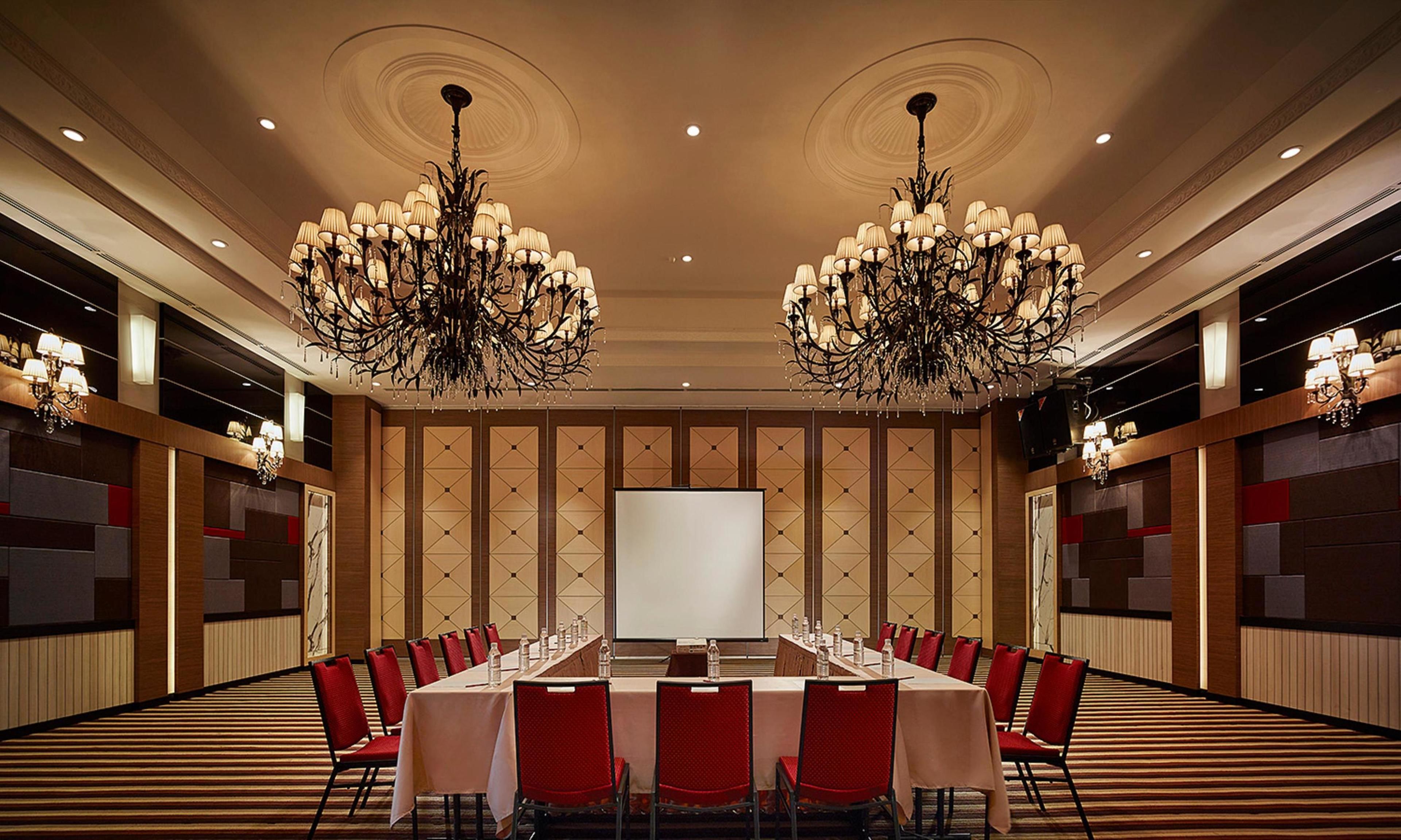 A conference room with a long table, red chairs, and chandeliers.