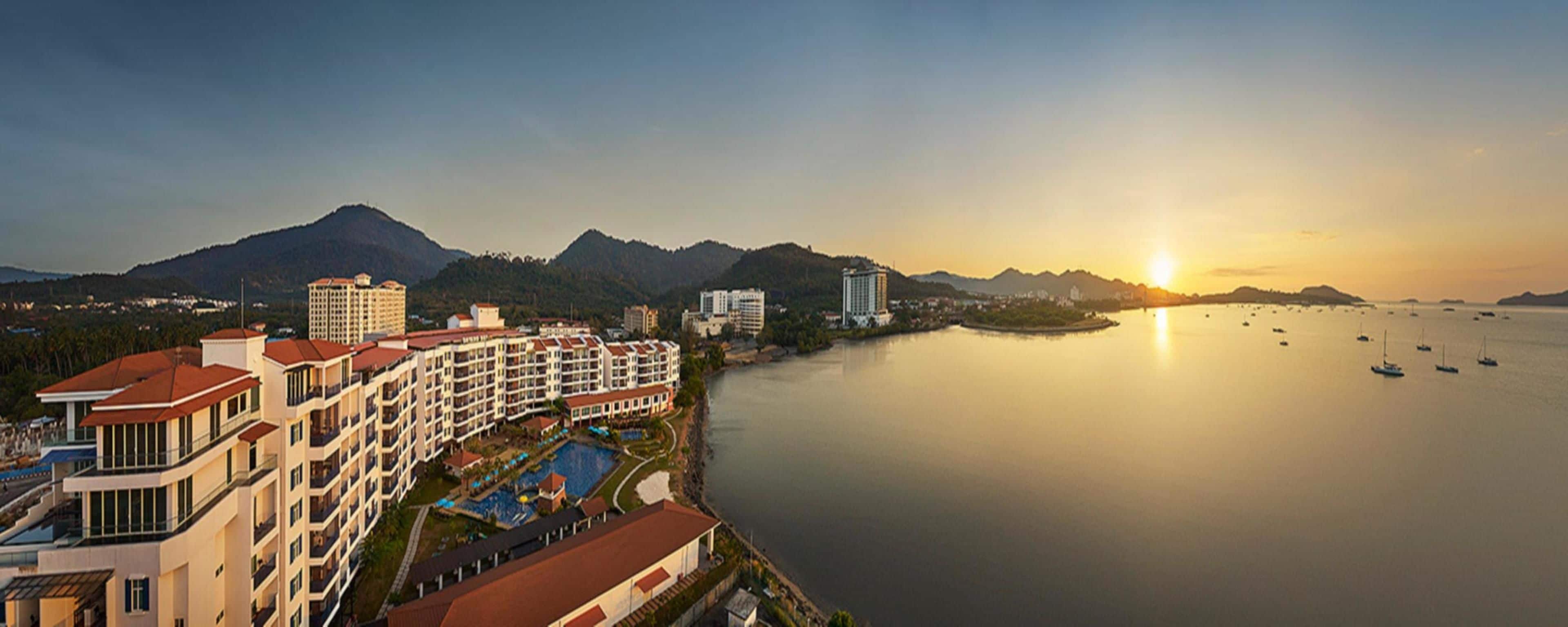 A coastal hotel with multiple buildings, a swimming pool, and a view of the sea with boats.