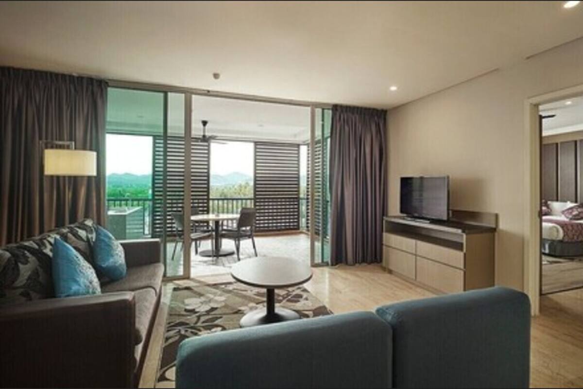 Une chambre d’hôtel moderne équipée d’un canapé, d’une petite table, d’une télévision et d’un balcon offrant une vue sur les montagnes.