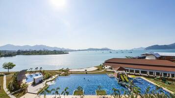 A resort with a large swimming pool, a water slide, and a view of the sea and mountains.