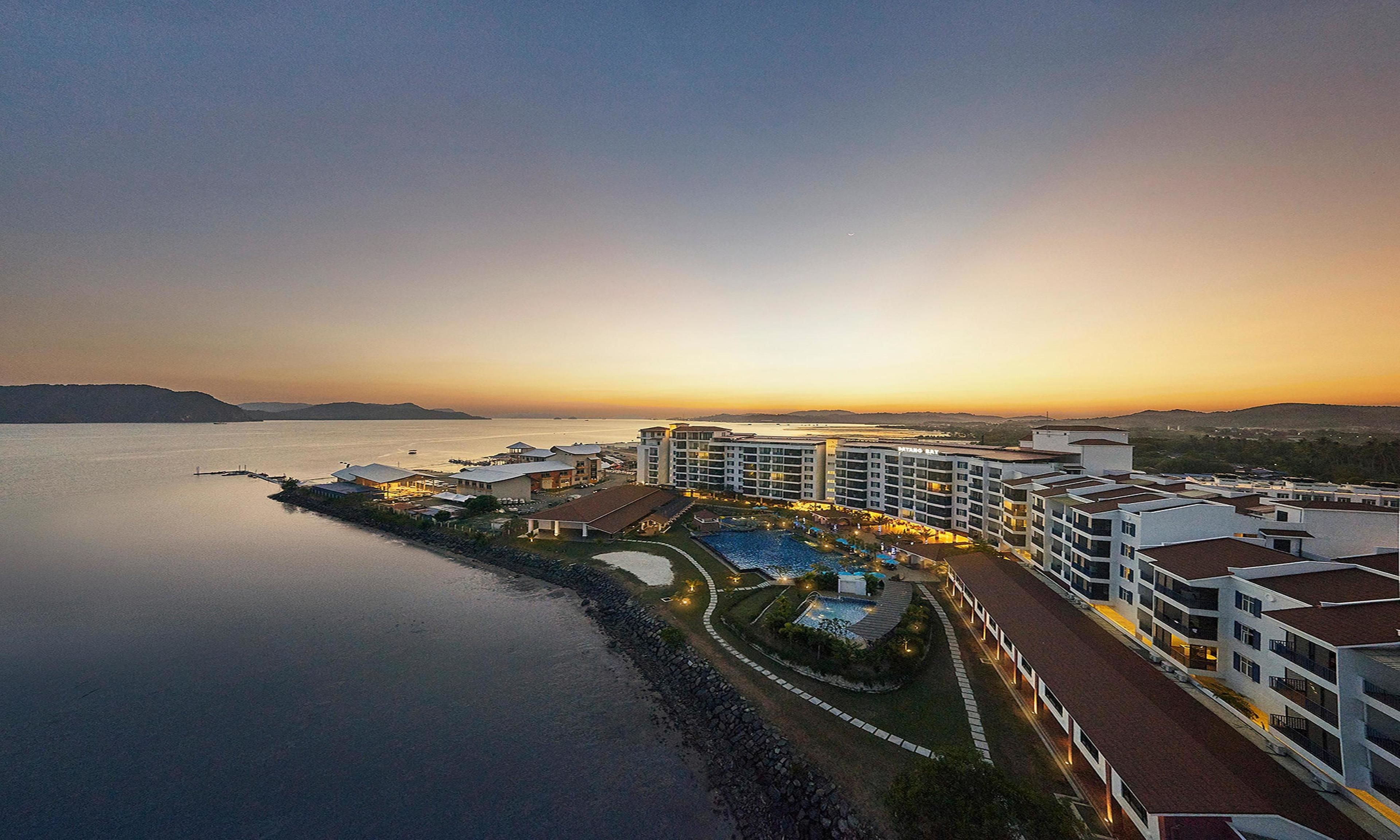 Un hôtel situé sur la côte, composé de plusieurs bâtiments, doté d’une piscine et offrant une vue sur la mer.